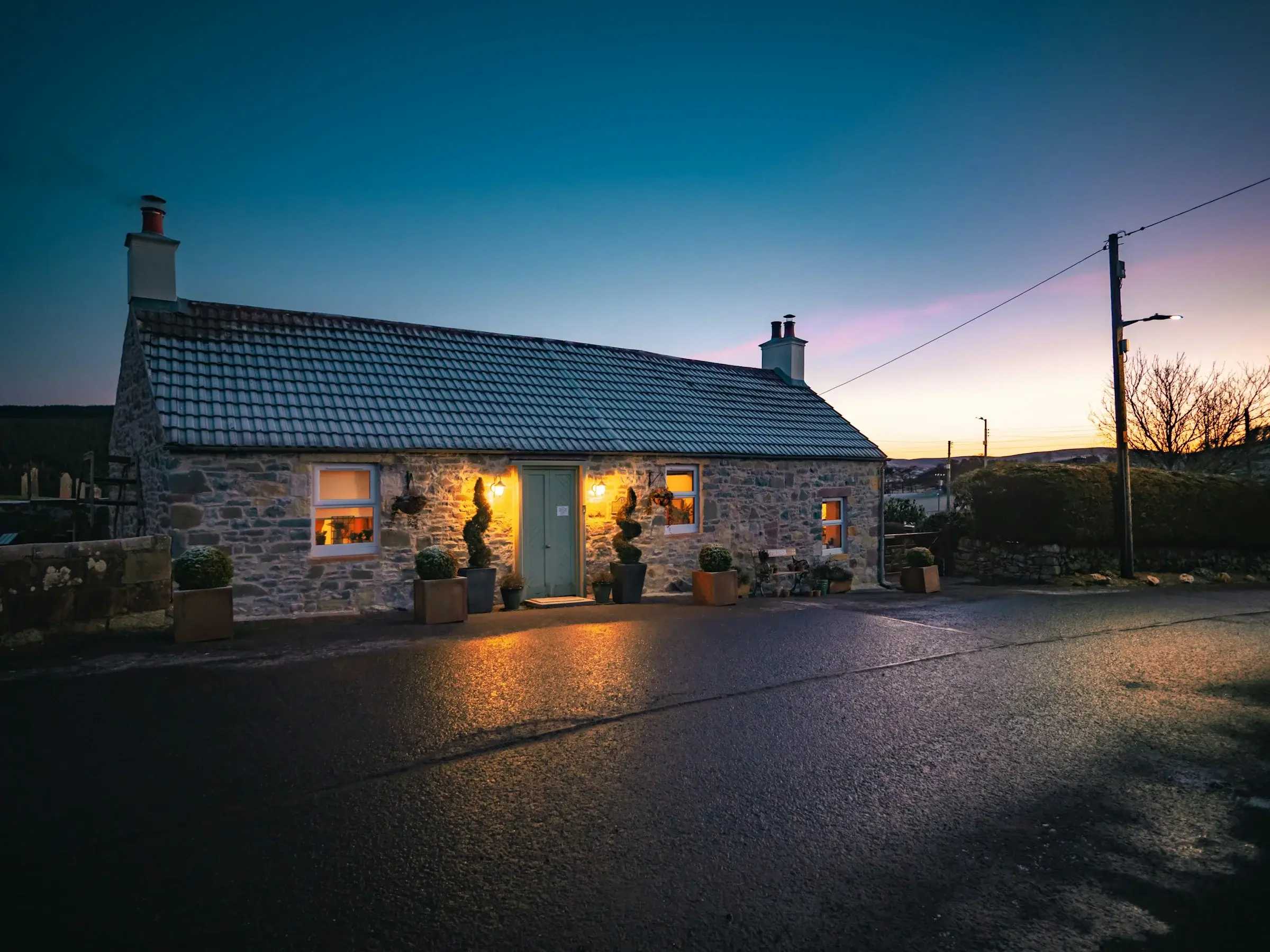 A stone cottage at dusk, its windows glowing warm against a deep twilight sky